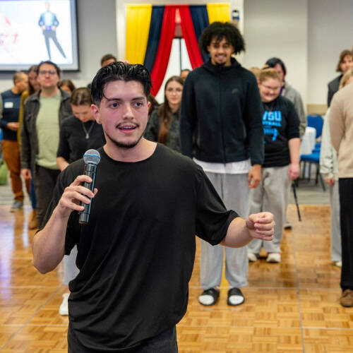 Daniel Lozano, with microphone, leads a dance class of people standing on a dance floor